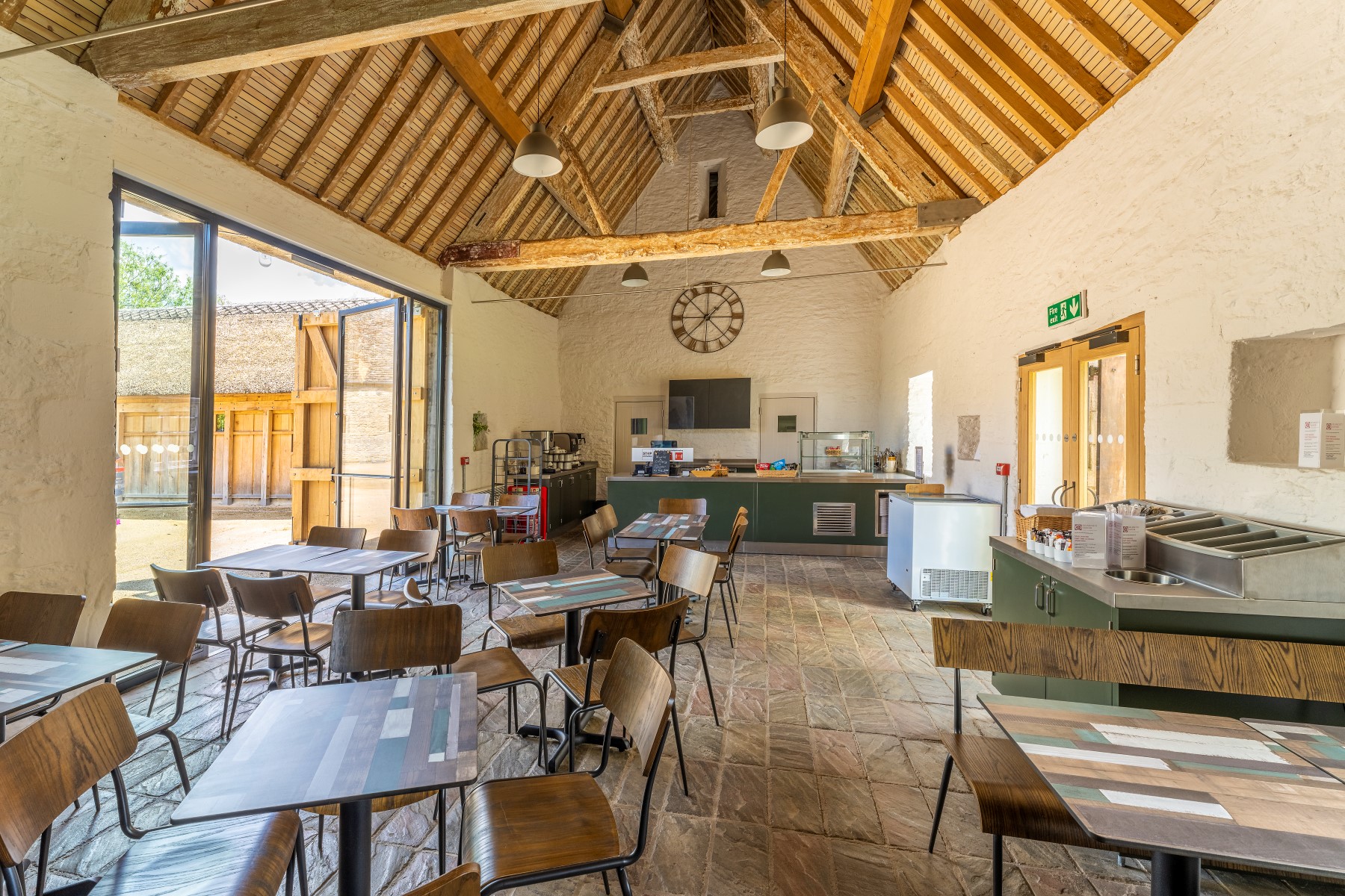 A large open space with high ceilings and wooden beams. Tables and chairs are over the barn and there is a counter at the back of the room for with cases for tea and treats.