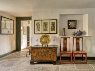 Garden hall at Kelmscott Manor with three framed drawings, chest with gold plate and chairs